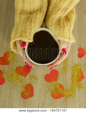 Cup of coffee or tea in womans's hands with good red manicure in knitted sweater