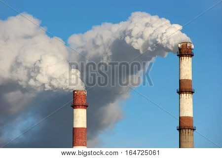 Dense clouds of smoke or steam out of two pipes on the background of blue sky. The concept of ecology pollution of the environment.