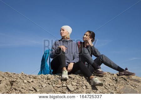 Two Woman Tourists With Backpacks Enjoying Sunset On Top Of A Mountain