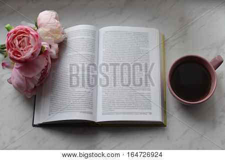 Cozy home still life: cup of hot coffee, spring flowers and opened book with warm plaid on windowsill. Springtime concept, free copy space.