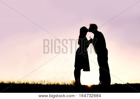 A silhouette of a happy young married couple in love kissing at sunset outside on a summer night.