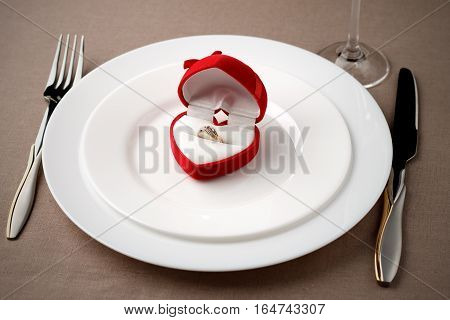 Golden Ring In Red Case On White Plate With Fork, Knife And Glass.