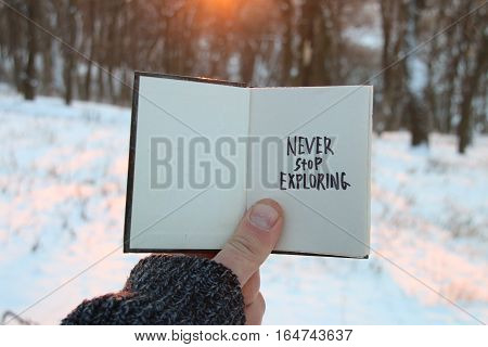 Never stop exploring. Inspirational and motivational quotes. Hand holding a book with the inscription.