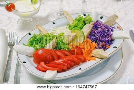 Raw salad on white plate with cutlery.