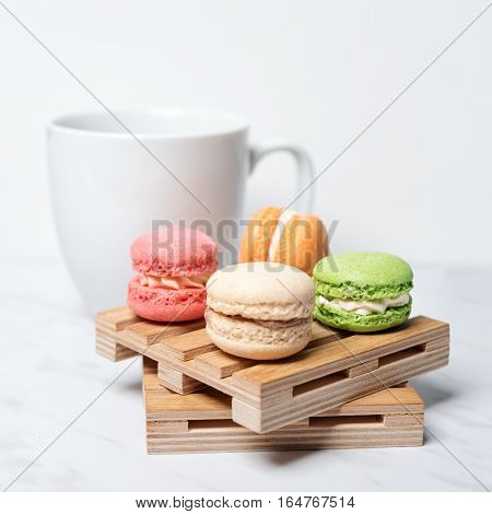Sweet and colourful macaroons served on little wooden pallets with cup of coffee on a marble texture background. Traditional french dessert