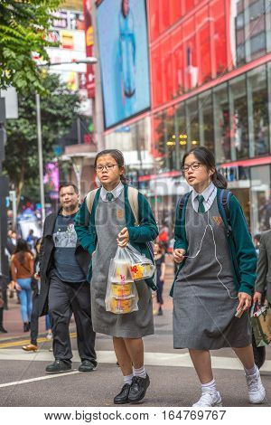 Hong Kong, China - December 6, 2016: typical asian school girls with clever look, carring food bag down the crowded street market Jardine's Crescent, Causaway Bay popular shopping district.