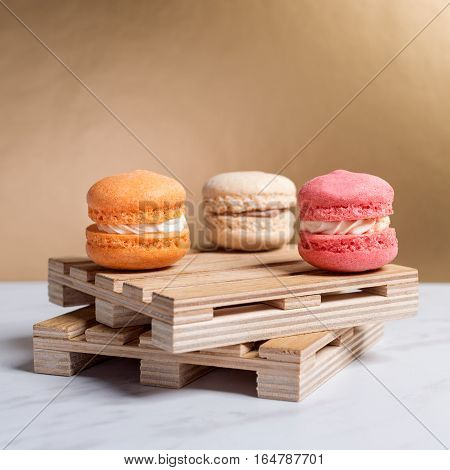 Sweet and colourful macaroons served on little wooden pallets on a marble texture table and golden background. Traditional french dessert. Copy space