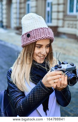 Beautiful girl photographer photographing the old town with retro camera. She is wearing a knitted cap