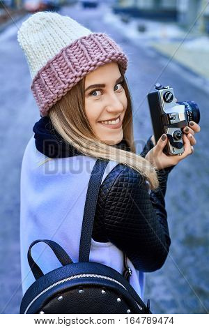 Beautiful girl photographer photographing the old town with retro camera. She is wearing a knitted cap
