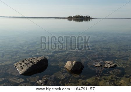 Dead calm afternoon image of shallow and clear lake huron water and limestone rocks along theshoreline. A small tree-covered island is on the horizon. Overall feeling is a calm peaceful tranquil serene and wild background.