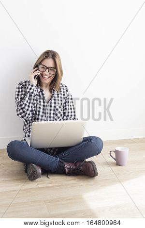 Young student working with computer and speaking with her smartphone