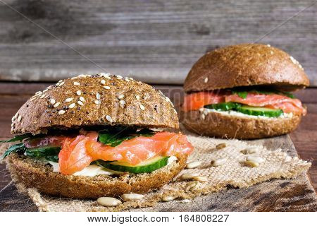 two sandwiches with cereals bread and smoked salmon with herbs cucumbers and cheese on wooden background with copy space for healthy breakfast. close up. shallow depth of field