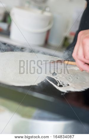 Spreading Crepe On Hot Griddle With A Wooden Scraper