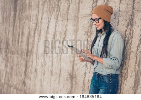 Modern Pretty Stylish Woman In Cap And Glasses Using Tablet Near Stone Wall
