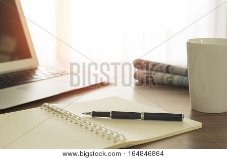 Notebook and pen on desk with tablet and offee cup and newpaper on the table in the morning.