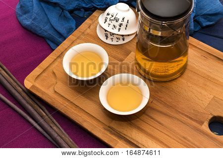 Green herbal tea in glass teapot on the blue wood background with aroma sticks and tea cup