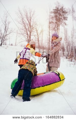 Group of happy chherful people having fun on snow hill. Two women and kid sliding on snow tubes. Winter vacation concept.