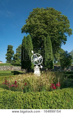 White sundial standing in the middle of a flowerbed.