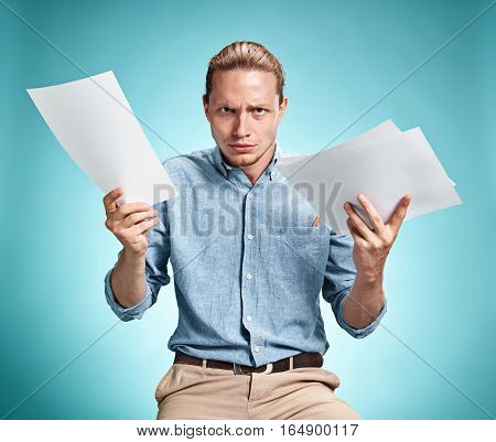Smart smiling student with great idea holding sheets of paper on blue studio background