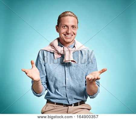 Happy excite young man in blue shirt smiling and celebrating his succcess over blue studio background