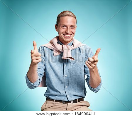Happy excite young man in blue shirt smiling and celebrating his succcess over blue studio background