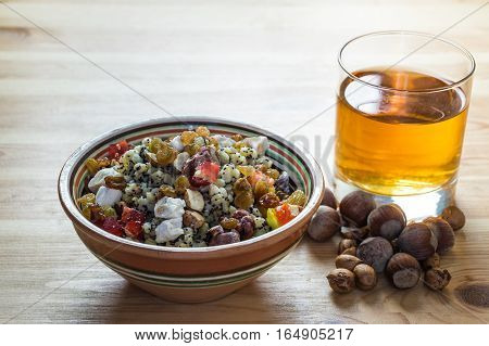 Ukrainian kutia and uzvar. Traditional christmas cereal wheat porridge with raisins, nuts, poppy seeds, honey and candied fruit in earthenware bowl with dried fruit drink on natural wood table