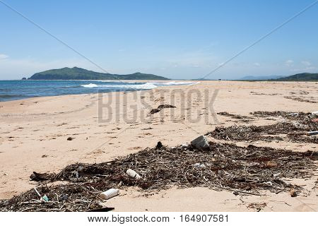 Various garbage on the sandy seashore thrown ocean waves. Yellow sand and blue sky. Wide angle.