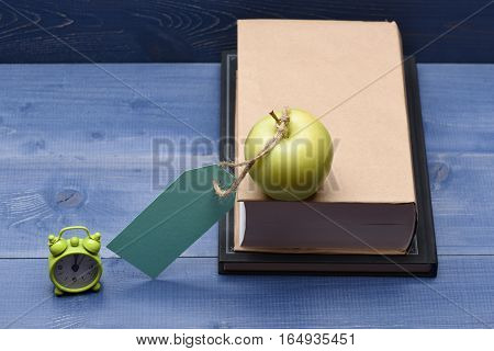 Books fresh green apple with turquoise tag string and alarm clock on blue vintage wooden background education concept copy space