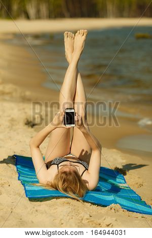 Summertime pleasures enjoying vacation concept. Woman in bikini sunbathing and relaxing on beach using smartphone checking social media and writing sms