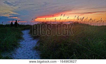 Couple watching sunset off a beach dune trail.