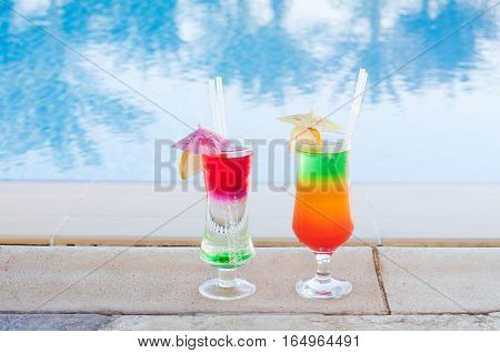 Colored cocktails on a background of water. Colorful cocktails near the pool. Beach party. Summer drinks. Exotic drinks. Glasses of cocktails on table near pool. Summer drinks photo concept. Сocktail