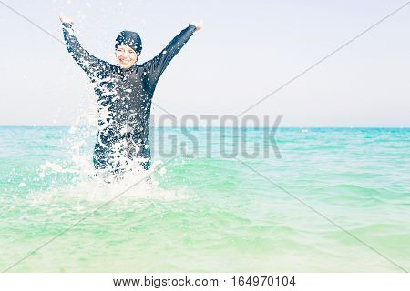young woman in burkini splashing water, persian gulf, jumeirah beach in dubai