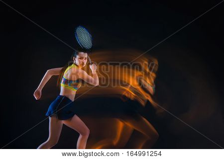 Portrait of beautiful girl tennis player with a racket on dark studio background. Stroboscope shooting technique