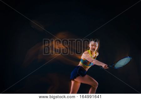 Portrait of beautiful girl tennis player with a racket on dark studio background. Stroboscope shooting technique