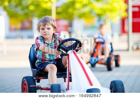 Two active little kid boys driving pedal race car in summer garden, outdoors. Children, best friends racing with fast speed and having fun. Twins making competition