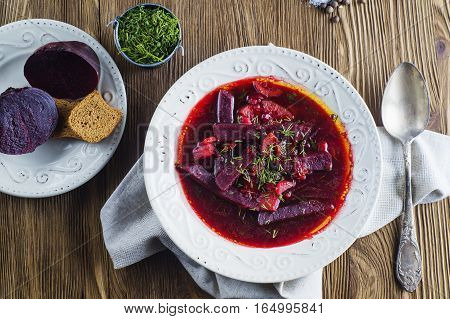 Vegetable soup - red borsch in a white bowl on a rustic wooden background top view. Healthy beetroot soup vegetarian food. Delicious beet soup with croutons flat lay.
