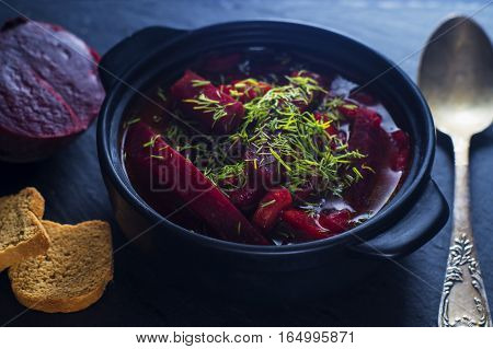 Vegetable soup - red borsch in the pot on a black slate board. Healthy beetroot soup vegetarian food. Delicious beet soup with croutons.