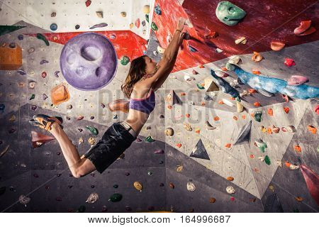 Free climber young woman climbing artificial boulder indoors