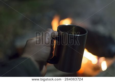 A Man Holds A Thermomug On The Background Of A Fire In Nature