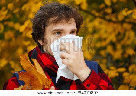 Man with cold rhinitis on autumn background. Fall flu season. Ill sick sneezing male. Handkerchief, vaccine against influenza virus Caught Cold Headache Allergy runny nose