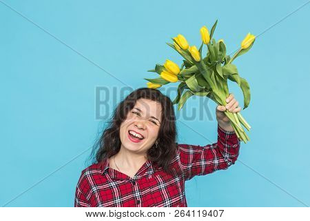 Laughing Young Caucasian Woman With Bouquet Of Tulips On Blue Background.