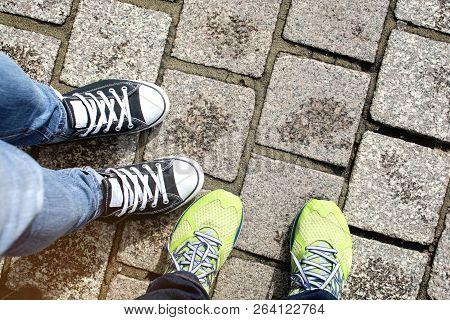 Two Pairs Of Running Shoe And Slipper Shoe Standing Together On Grey Brick Walkway, Tourist Couple T