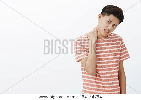 Portrait Of Bothered Uneasy Young Asian Man In Striped T-shirt Unwilling To Do Something Rubbing Nec