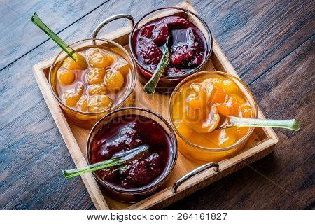 Various Glass Bowl Of Fruit Jams Apricot, Cherry, Strawberry, Damson Plum In Wooden Tray.