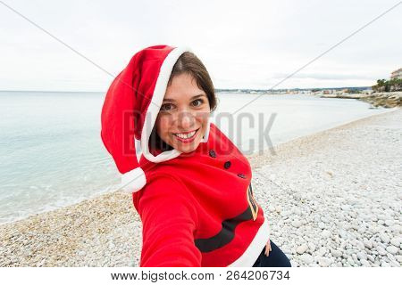 Christmas, Humor And People Concept - Young Woman In Santa Suit Making Selfie Near The Sea At Summer