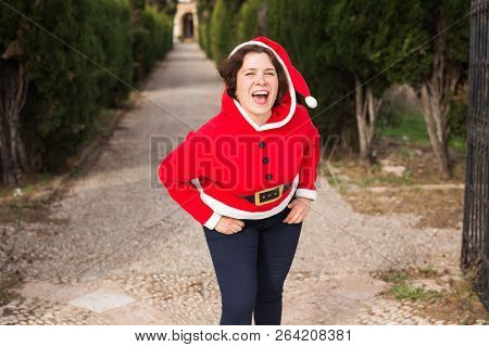 Christmas, Holidays, Humor And People Concept - Funny Happy Woman In Santa Suit Dancing Outdoors