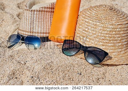 Two Sunhats, Sunglasses And Sunprotection Cream Are Laying On The Sand.