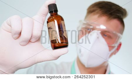 A Young Professional Master Holds A Jar In A White Coat, Safety Goggles, White Rubber Gloves.
