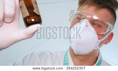 A Young Professional Master Holds A Jar In A White Coat, Safety Goggles, White Rubber Gloves.