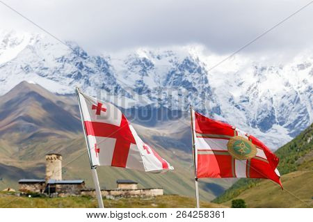 Flying Flag Of Georgia And Flag Of Georgian Border Police. With Svans Tower And Mountains On The Bac
